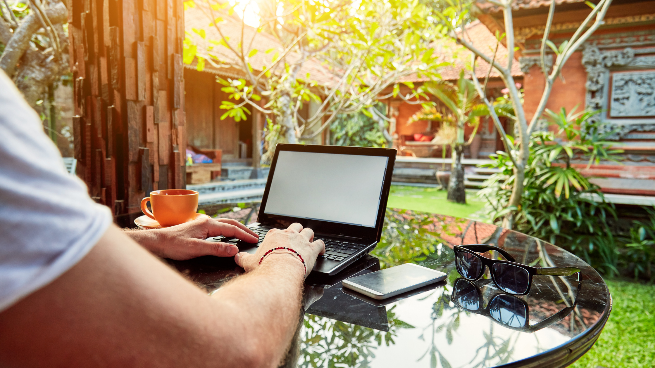 Mann am Tisch mit Laptop in einem grünen Garten hinter einem Haus