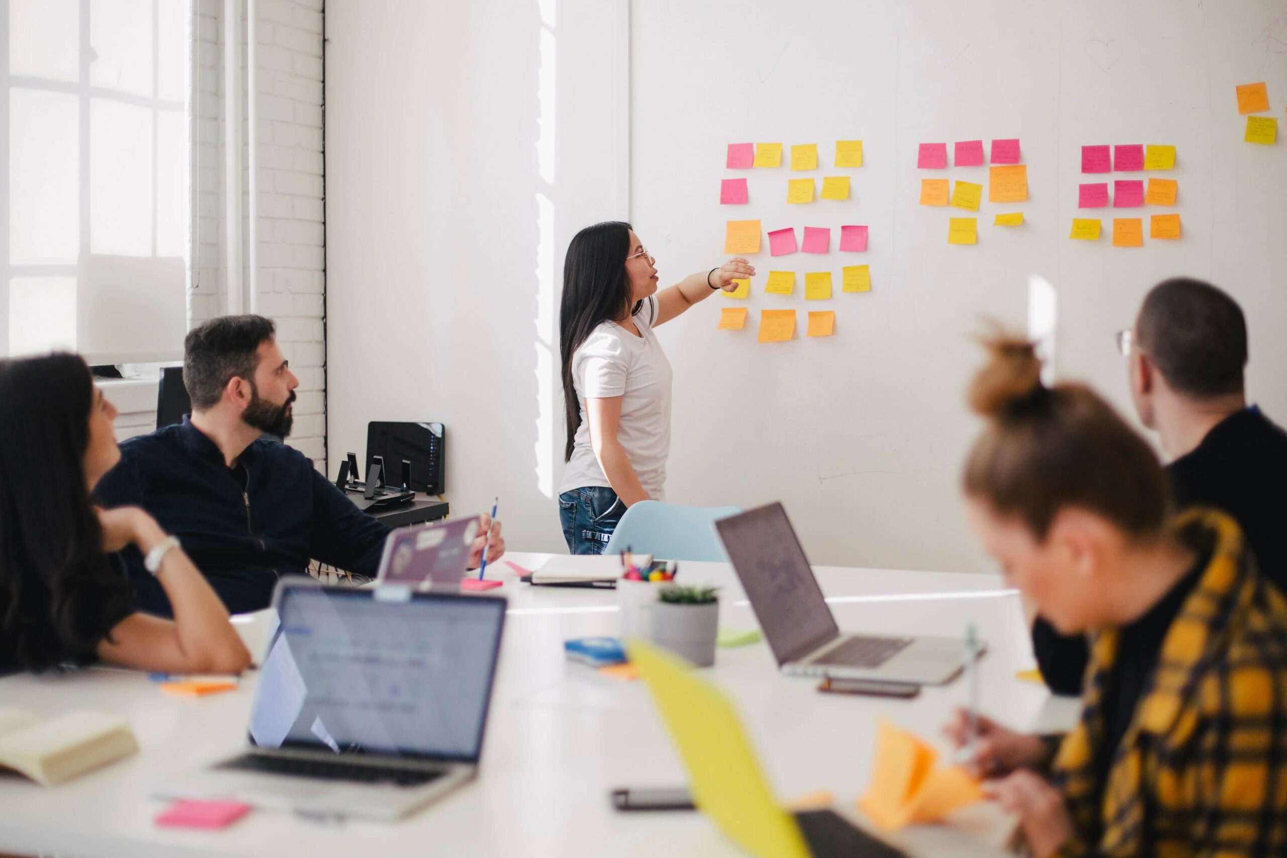 Team mit Laptops, Frau an Planwand mit Post It Notes