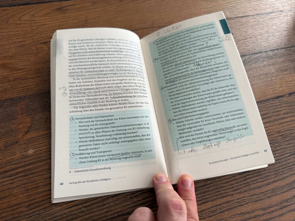 Der Alt-Text für das Bild könnte wie folgt lauten:

"Eine Person hält ein aufgeschlagenes Buch mit dem Titel 'Künstliche Intelligenz und Ethik' in den Händen. Die Seiten des Buches sind sichtbar und zeigen Text sowie hervorgehobene Abschnitte in hellblauer Farbe. Die linke Seite enthält eine Liste mit Punkten zum Thema Vertraulichkeit und Datenschutz im Zusammenhang mit KI, während die rechte Seite Fragen zur Verantwortung und Kompetenz in der Beratung durch KI behandelt. Das Buch liegt auf einem Holztisch."